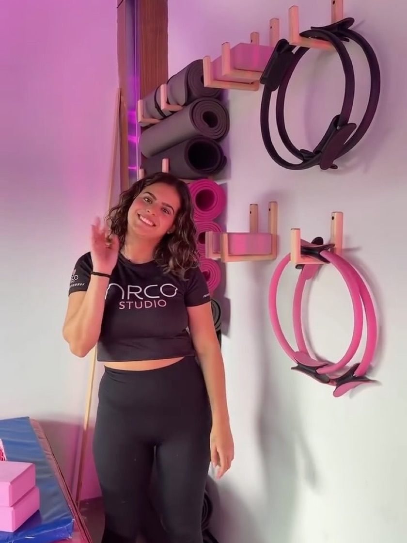 Instructora junto al muro de material de pilates del estudio.
